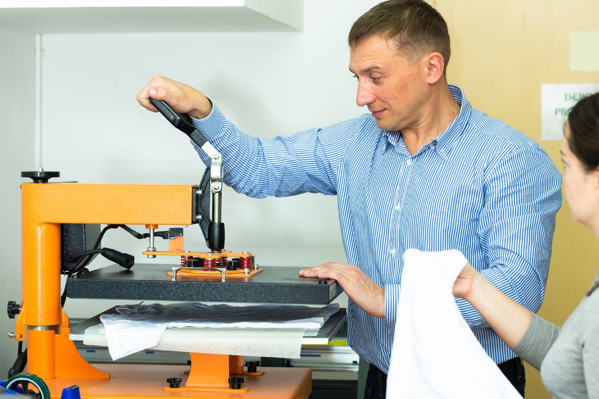 A person printing t-shirt under a machine.