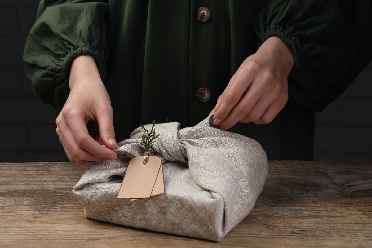 A lady wrapping a gift item with a clothing material to give it a personalized touch.