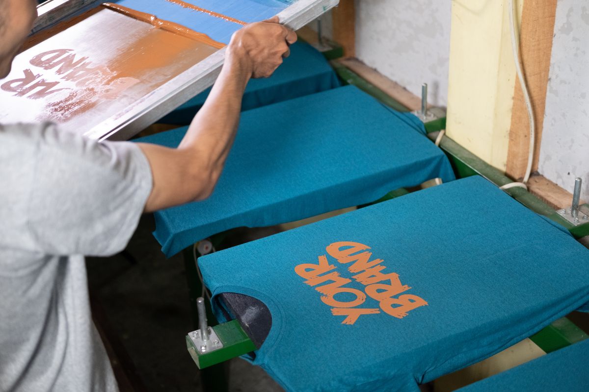 A person printing on large number of t-shirt to meet customer need.