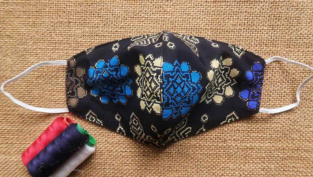 An embroidered face mask is shown in the image, with some sewing spools kept beside it