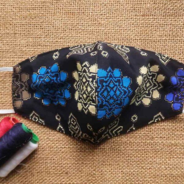 An embroidered face mask is shown in the image, with some sewing spools kept beside it