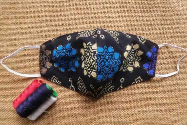 An embroidered face mask is shown in the image, with some sewing spools kept beside it