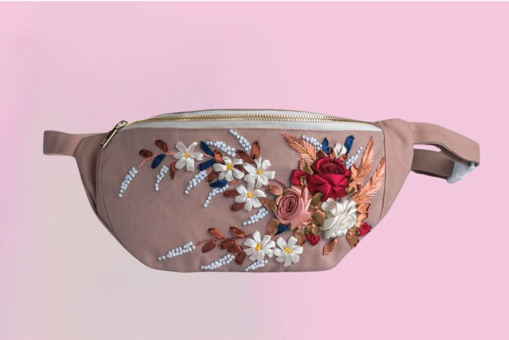 An embroidered fanny pack with some flowers embroidered on it.