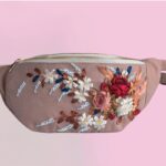 An embroidered fanny pack with some flowers embroidered on it.