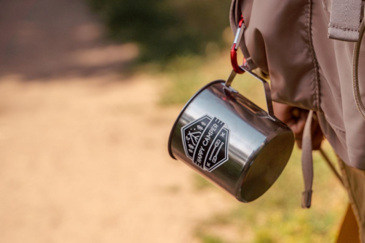 A person carrying a bag with a travel mug attached to it
